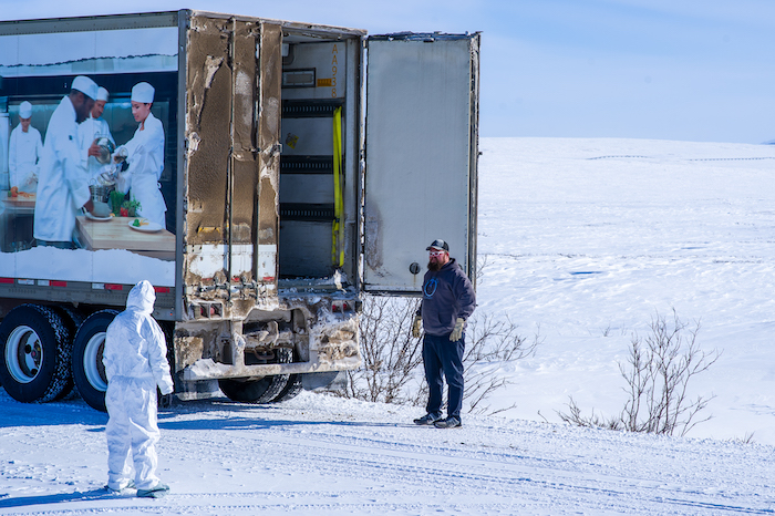 Figure 1. Gina Carani, Sous Chef, dressed in protective gear receiving a food delivery. Once the food (or any kind of delivery) was unloaded TFS staff in protective gear would move it to a quarantine location for three days prior to distribution. Photo courtesy of Joe Franich.