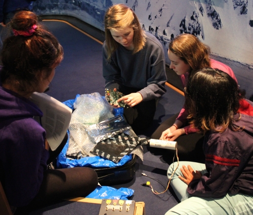  After their presentation on the IceCube observatory, Claire Hacker and Anna Caldwell-Overdier demonstrate cosmic-ray detector equipment to a couple of the Chilean students.  Photo courtesy of Lynn Foshee Reed.