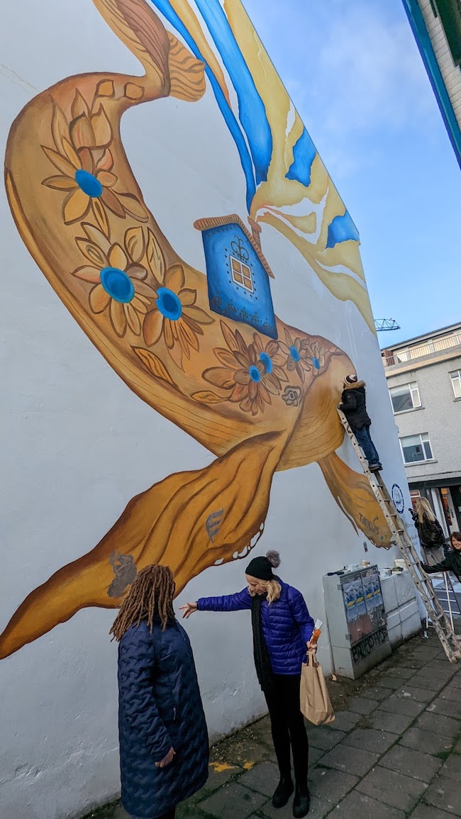 Figure 2b. Sveta Yamin-Pasternak with Olga Yakuba of Odesa, Ukraine, the project lead on the mural &quot;Our Love is as Big as a Whale,&quot; painted by a group of Ukrainian refugees with the participation of Odesa&#39;s Studio Peach and President of Iceland, Guðni Thorlacius Jóhannesson. Photo courtesy of Igor Pasternak.